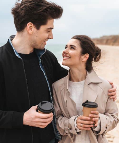 Beeld van een stel met dat naar elkaar kijkt en samen loopt op het strand. Zij brengen tijd samen (quality time) door wat belangrijk is als het gaat om een sterke relatie.