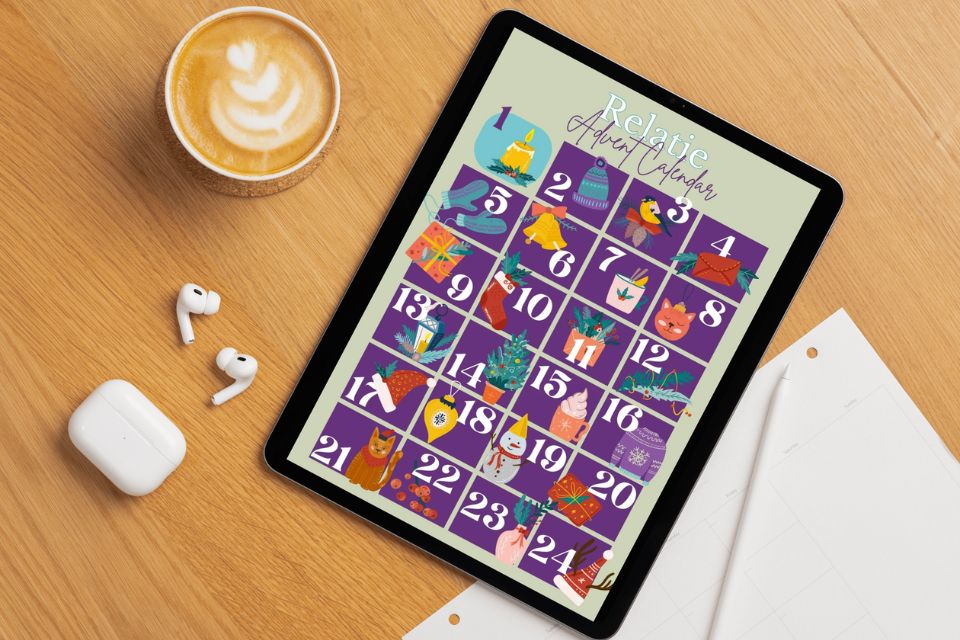 Foto van een tablet met op een tafel met oortjes, papier, pen en kop koffie. Op de tablet is de Relatie Adventskalender te zien.