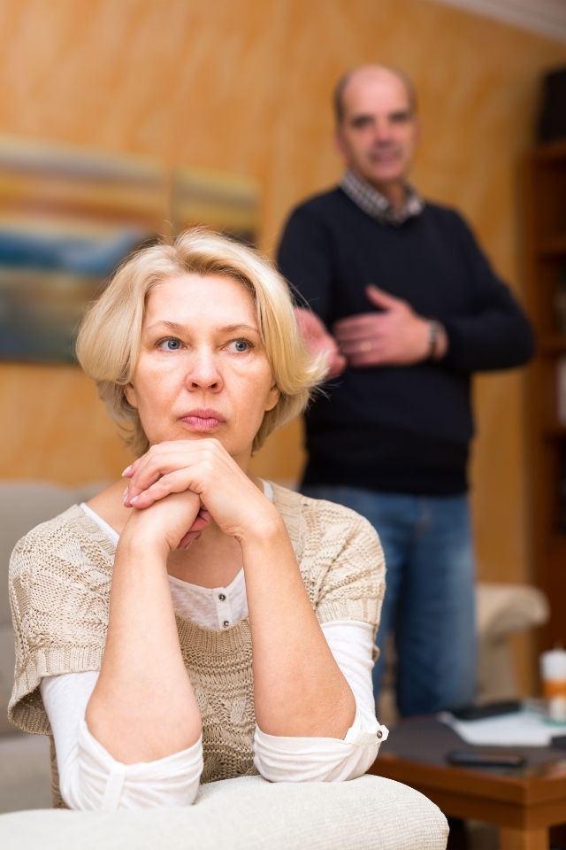 Afwezige blik bij vrouw terwijl partner op de achtergrond staat – voorbeeld van een relatie waarin geen bereidheid is om verder te investeren.